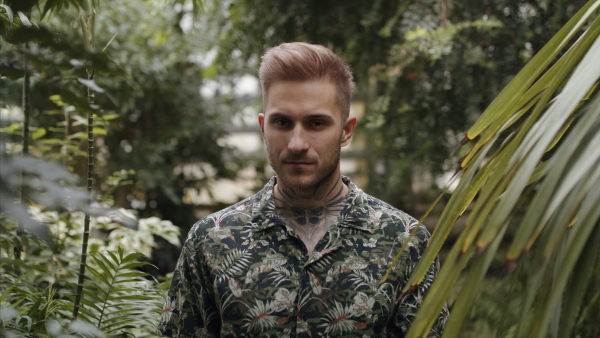 Attractive young man standing in botanical garden, looking at camera.