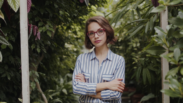 Beautiful young woman standing in botanical garden, looking at camera.