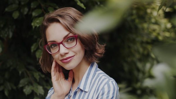 Beautiful young woman standing in botanical garden, looking at camera.