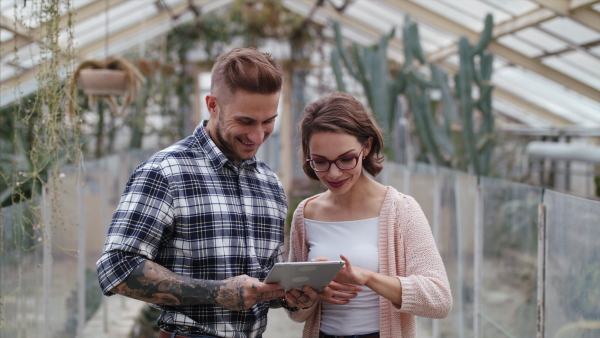 Man and woman researchers standing in greenhouse in botanical garden, using tablet.