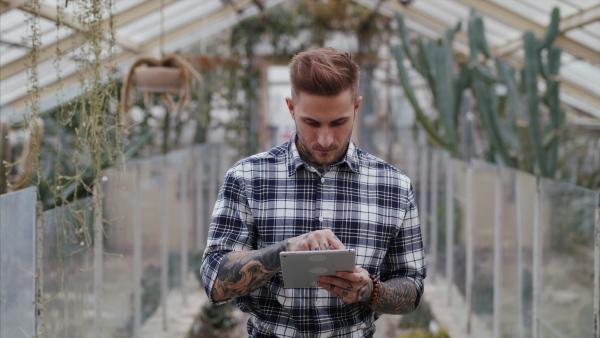 Man researcher standing in greenhouse in botanical garden, using tablet.