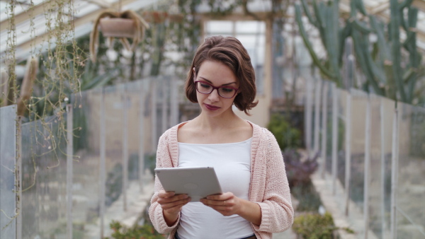 A young woman researcher standing in greenhouse, using tablet.