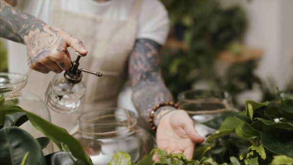 Midsection of unrecognizable man florist standing in flower and plant shop, spraying plants with water.