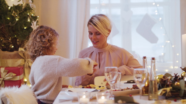 Happy small girl with mother at the table indoors at Christmas time, talking.