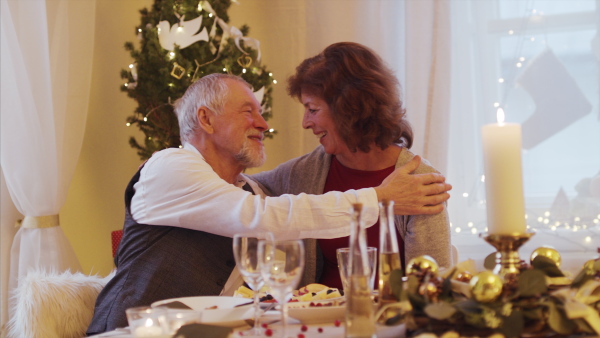 Happy senior couple in love indoors at home sitting at the table at Christmas, hugging and talking.