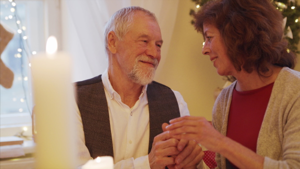 Happy senior couple in love indoors at home sitting at the table at Christmas, talking.