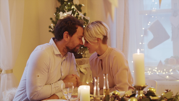 Portrait of happy couple in love indoors at the table celebrating Christmas, talking.