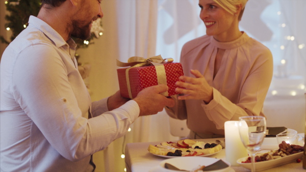 Portrait of happy couple indoors at the table celebrating Christmas, giving presents.