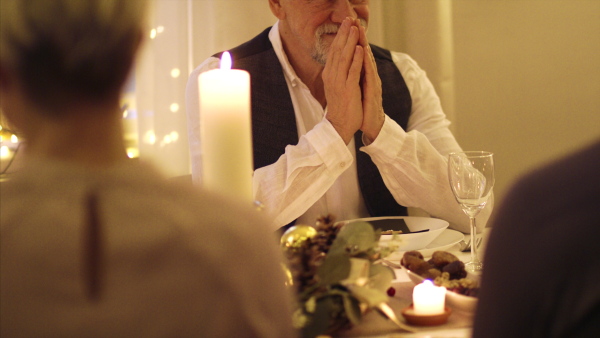 Happy senior man with family sitting at the table indoors at Christmas, dinner and praying concept.