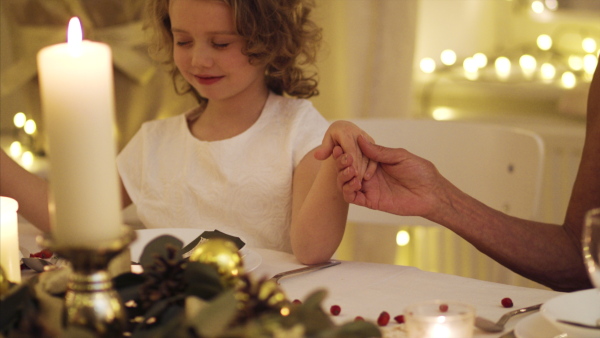 Small girl with grandmother holding hands together at the table indoors at Christmas, praying concept.