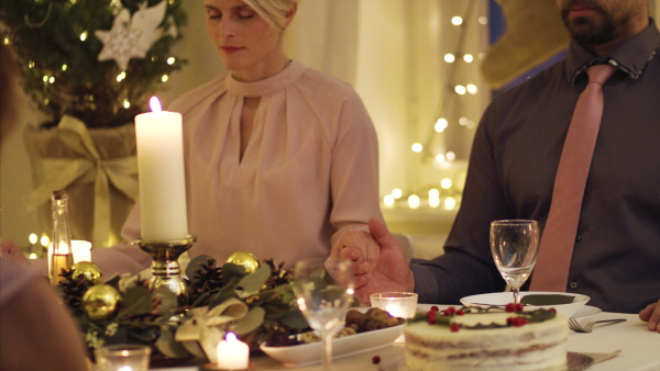 Mature couple with closed eyes holding hands together at the table at Christmas, praying concept.