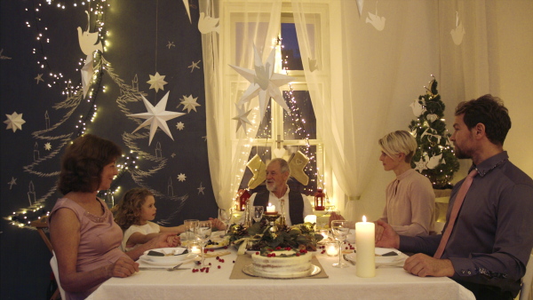 Multi-generation family indoors celebrating Christmas together, holding hands and talking.