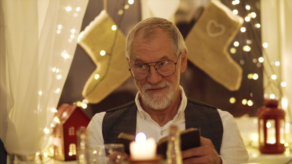 Senior man sitting with family at the table indoors at Christmas, dinner and bible reading concept.