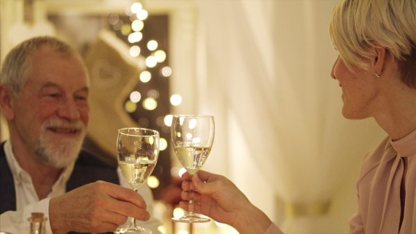 Happy senior man with family sitting at the table indoors at Christmas, clinking glasses with wine.