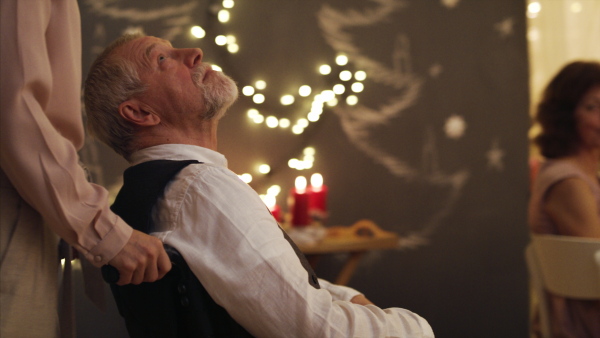 Happy senior man in wheelchair with family indoors at Christmas, dinner concept.