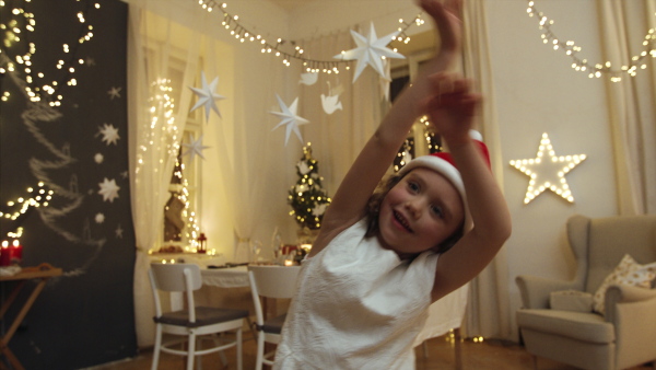 Portrait of cheerful small girl standing indoors at Christmas, dancing.