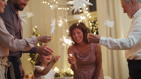 Happy small girl with parents and grandparents indoors celebrating Christmas, holding sparklers.