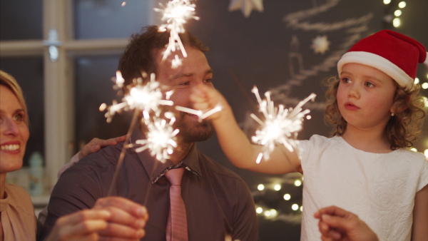 Happy small girl with parents indoors celebrating Christmas, holding sparklers.