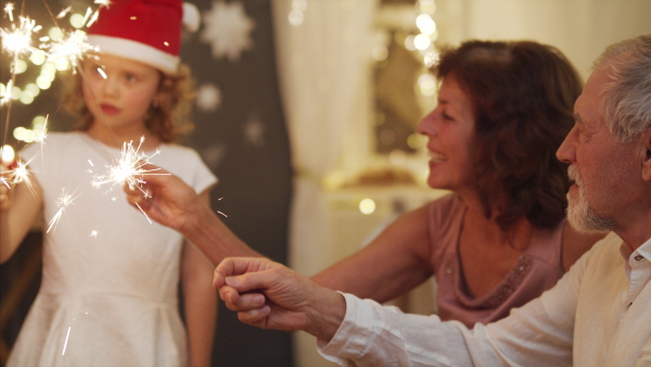 Happy small girl with grandparents indoors celebrating Christmas, holding sparklers.