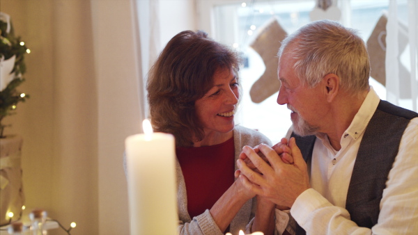 Happy senior couple in love indoors at home sitting at the table at Christmas, talking.