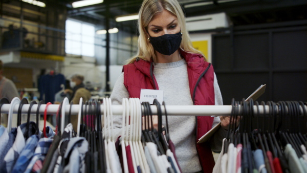 Woman volunteer working with clothes in community charity donations center, coronavirus concept.