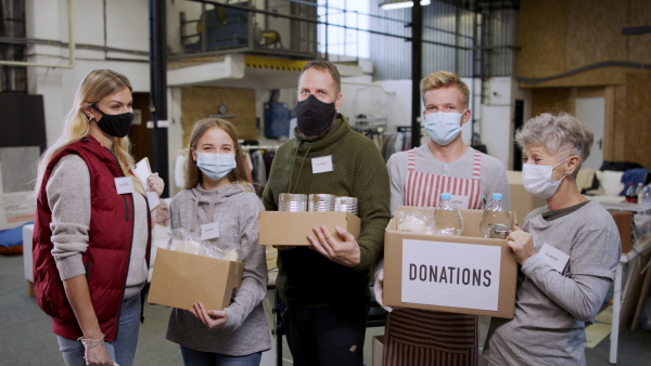 Group of volunteers with boxes looking at camera in community charity donation center, coronavirus concept.