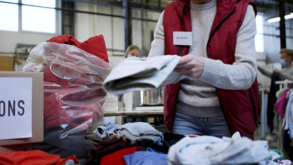 Portrait of unrecognizable volunteers sorting out donated clothes in community charity donation center.