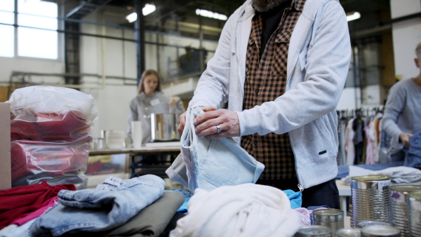 Portrait of unrecognizable volunteers sorting out donated clothes in community charity donation center.