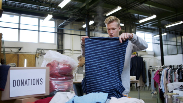 Portrait of volunteers sorting out donated clothes in community charity donation center, looking at camera. Coronavirus concept.