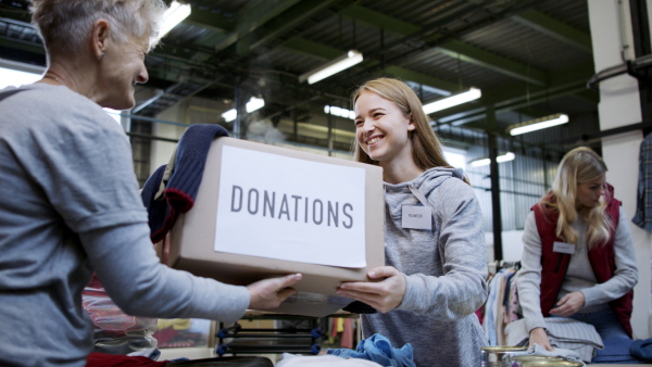 Portrait of volunteers sorting out donated clothes in community charity donation center, coronavirus concept.