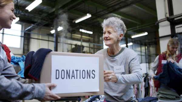 Portrait of volunteers sorting out donated clothes in community charity donation center, coronavirus concept.