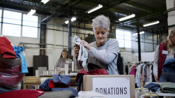 Portrait of volunteers sorting out donated clothes in community charity donation center, looking at camera. Coronavirus concept.