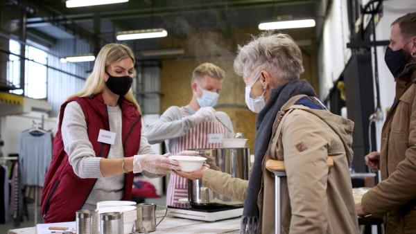 Volunteers serving hot soup for ill and homeless in community charity donation center, food bank and coronavirus concept.