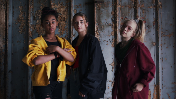 Front view of group of teenagers girl gang standing indoors in abandoned building, hanging out.