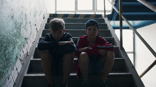 Teenagers boys indoors in abandoned building, sitting on stairs and looking at camera.