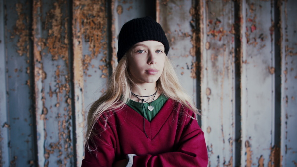 Front view portrait of blond teenager girl standing indoors in abandoned building.