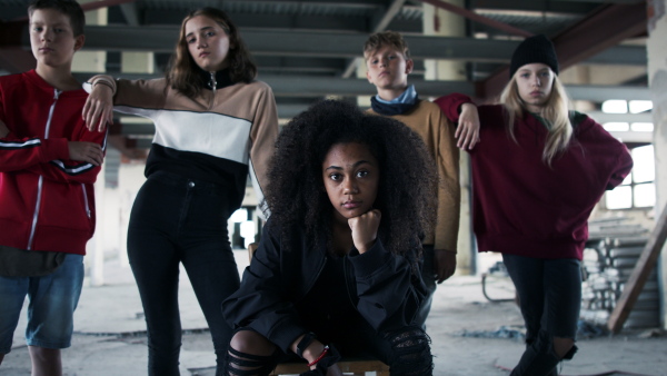 Front view of group of teenagers gang standing indoors in abandoned building, looking at camera.