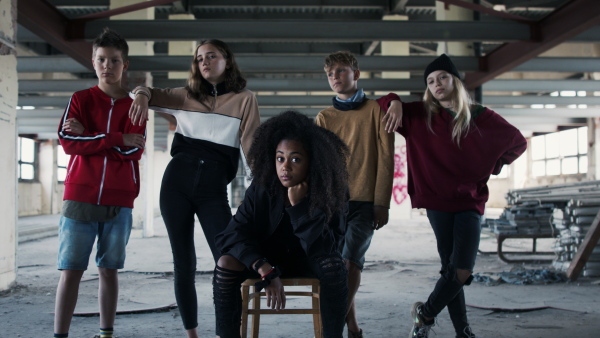 Front view of group of teenagers gang standing indoors in abandoned building, looking at camera.