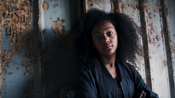 Front view portrait of mixed- race teenager girl standing indoors in abandoned building.