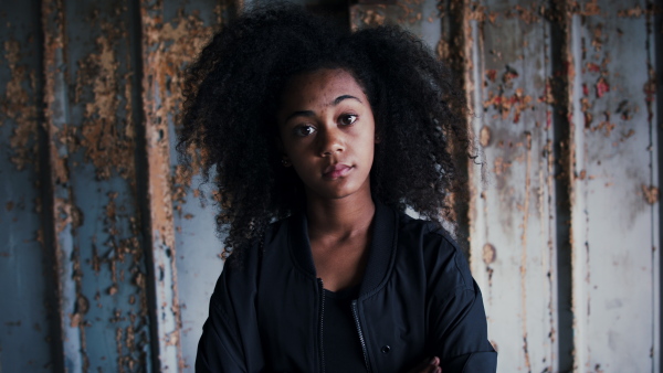 Front view portrait of mixed- race teenager girl standing indoors in abandoned building.