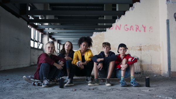 Front view of group of teenagers gang standing indoors in abandoned building, looking at camera.