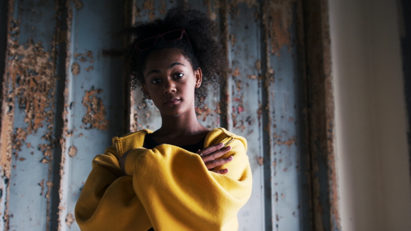 Front view portrait of mixed- race teenager girl standing indoors in abandoned building.