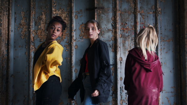 Front view of group of teenagers girl gang standing indoors in abandoned building, hanging out.