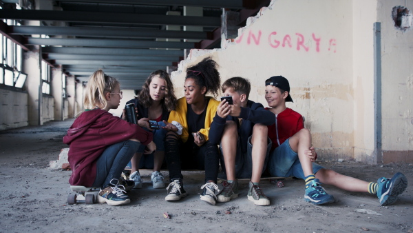 Front view of group of teenagers gang with smartphone talking indoors in abandoned building, looking at camera.