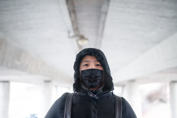 Man in black clothes and mask standing outdoors in city, coronavirus concept. Copy space.