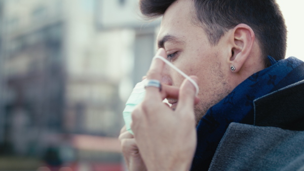 Close-up of man putting on face mask outdoors in city, coronavirus and protection concept.