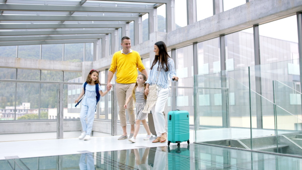 Happy family with two children going on holiday, walking at the airport with luggage.