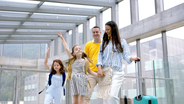 Happy family with two children going on holiday, walking at the airport with luggage.