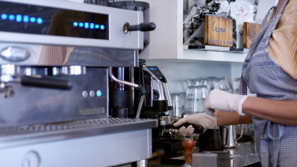 Unrecognizable woman barista working with gloves in coffee shop, making coffee.