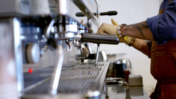 Unrecognizable man barista working with gloves in coffee shop, disinfecting machine.